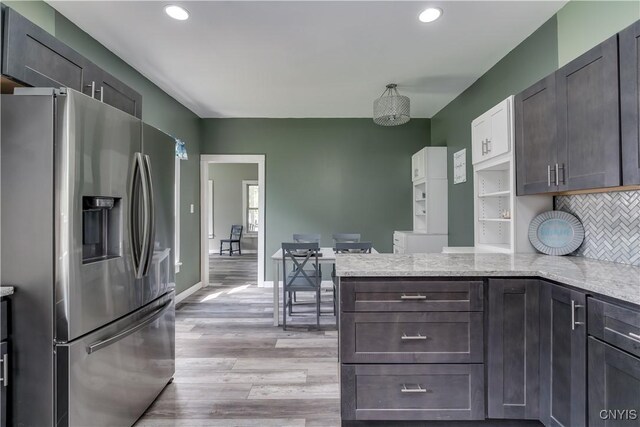 kitchen with light wood-type flooring, decorative backsplash, dark brown cabinetry, light stone countertops, and stainless steel fridge