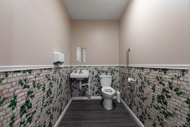 bathroom featuring wood-type flooring, toilet, a textured ceiling, and tile walls