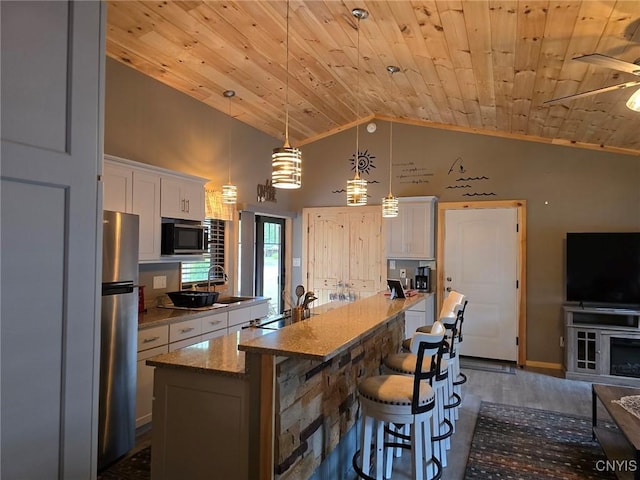 kitchen featuring white cabinetry, a center island with sink, stainless steel fridge, light stone countertops, and pendant lighting