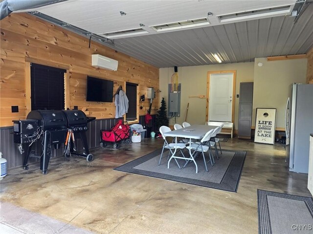 garage with wood walls, electric panel, an AC wall unit, and stainless steel refrigerator