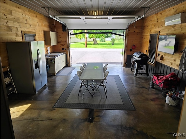 garage featuring sink, wooden walls, stainless steel fridge with ice dispenser, and a wall mounted air conditioner