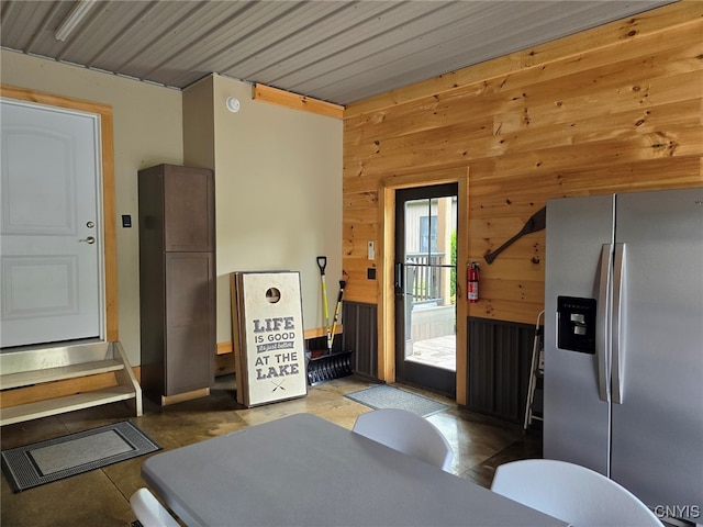 kitchen featuring stainless steel fridge, wooden walls, and light tile patterned flooring