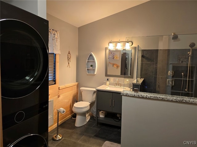 bathroom with stacked washing maching and dryer, tile patterned floors, vanity, toilet, and walk in shower