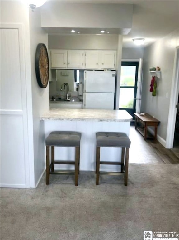 kitchen featuring a kitchen bar, sink, white refrigerator, kitchen peninsula, and white cabinets