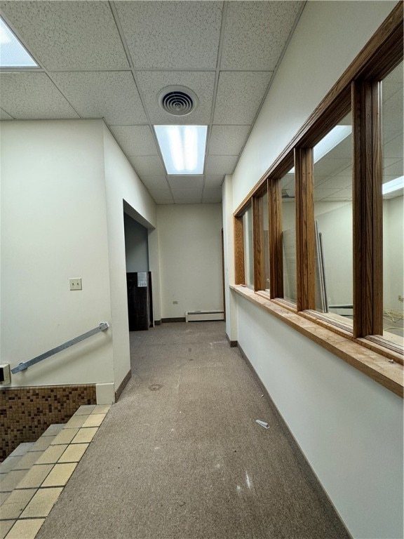 hall with a baseboard radiator, a drop ceiling, and light carpet