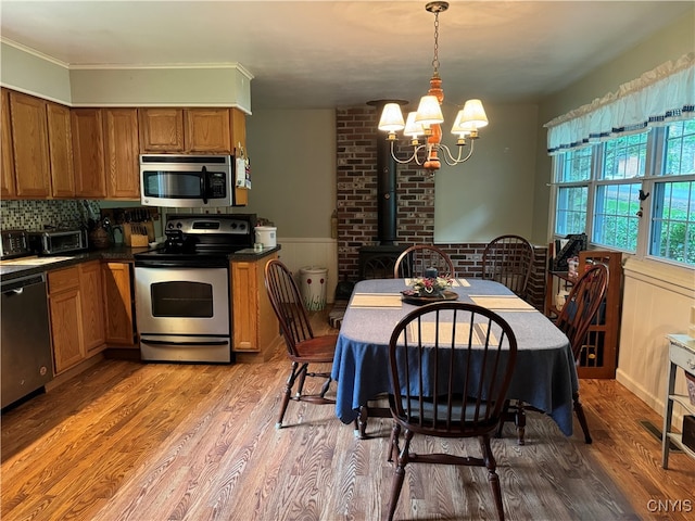 kitchen with appliances with stainless steel finishes, hardwood / wood-style floors, a chandelier, brick wall, and a wood stove