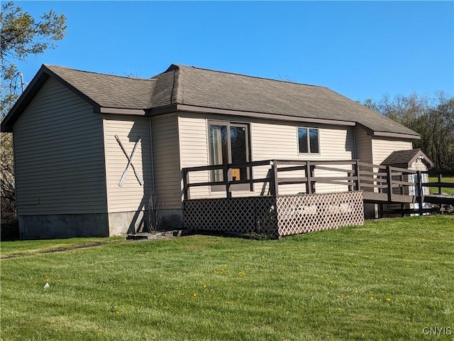 rear view of house with a shingled roof, a deck, and a lawn