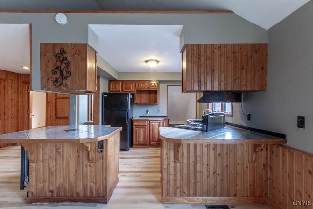 kitchen featuring black refrigerator, kitchen peninsula, light hardwood / wood-style flooring, and tile counters