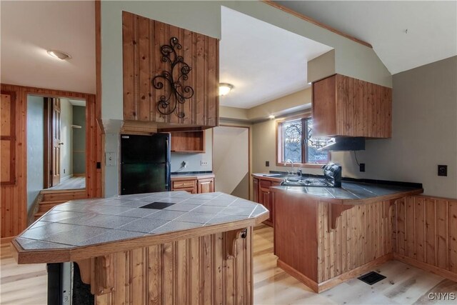 kitchen with black refrigerator, kitchen peninsula, light hardwood / wood-style flooring, and tile countertops