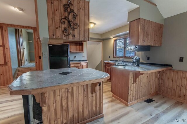 kitchen with sink, black refrigerator, light wood-type flooring, tile counters, and a breakfast bar