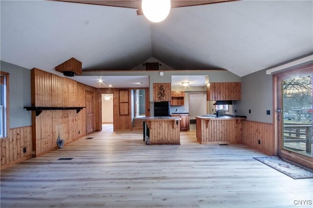 kitchen with black fridge, light wood-type flooring, wood walls, and a center island