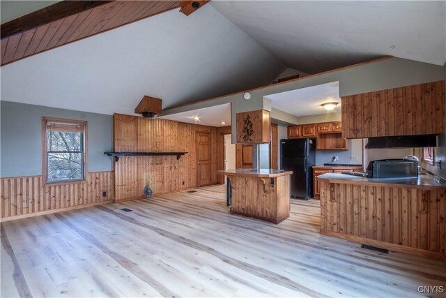 kitchen with light wood-type flooring, black refrigerator, lofted ceiling with beams, and wood walls