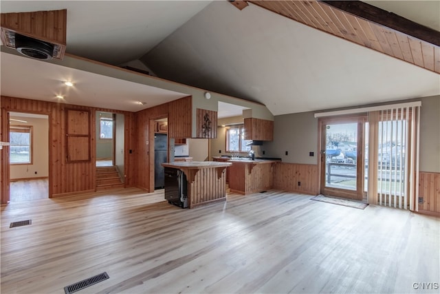 kitchen featuring a breakfast bar, light wood-type flooring, vaulted ceiling, wooden walls, and kitchen peninsula