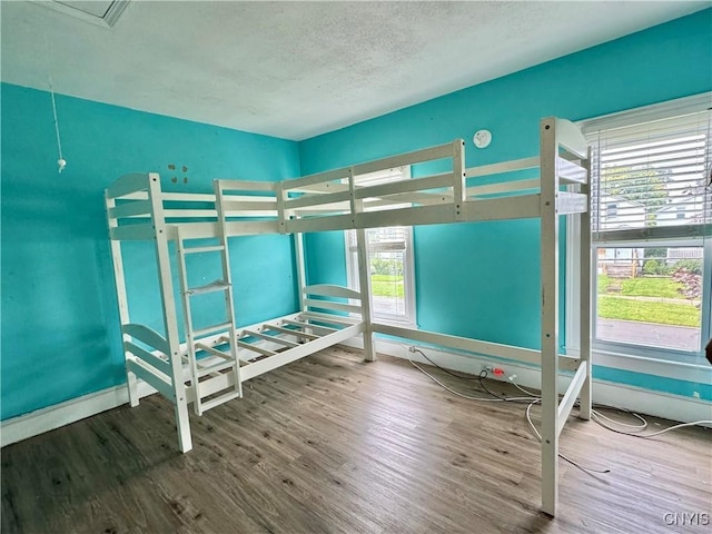 unfurnished bedroom featuring a textured ceiling, multiple windows, wood finished floors, and baseboards