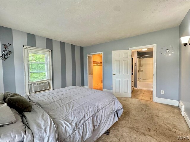 bedroom featuring a textured ceiling, a walk in closet, a closet, ensuite bath, and light colored carpet