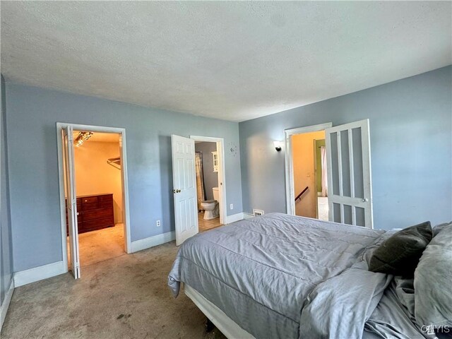 bedroom with ensuite bath, light carpet, a textured ceiling, and a spacious closet