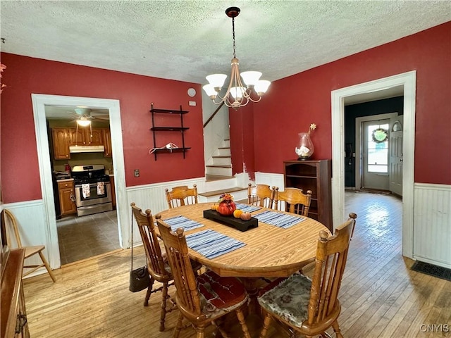 dining area featuring a textured ceiling, a notable chandelier, stairway, wainscoting, and wood-type flooring