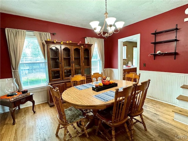 dining area featuring light wood finished floors, a textured ceiling, a notable chandelier, and wainscoting