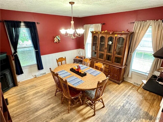 dining room with light wood-type flooring, a textured ceiling, and a chandelier