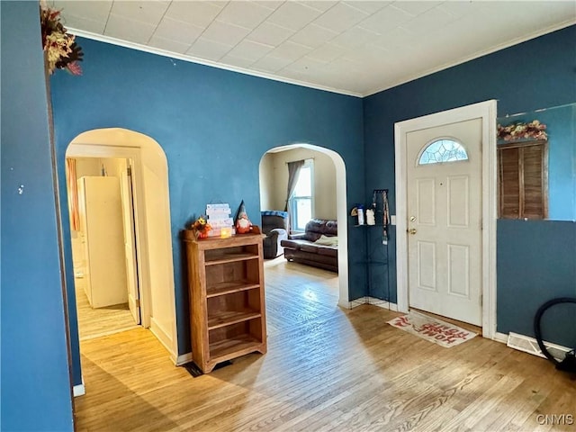 entrance foyer featuring baseboards, crown molding, arched walkways, and wood finished floors