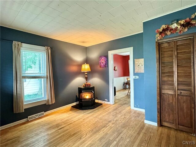 unfurnished room featuring hardwood / wood-style floors, a wood stove, ornamental molding, and a healthy amount of sunlight