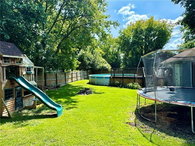 view of yard featuring a trampoline, a playground, and a fenced in pool