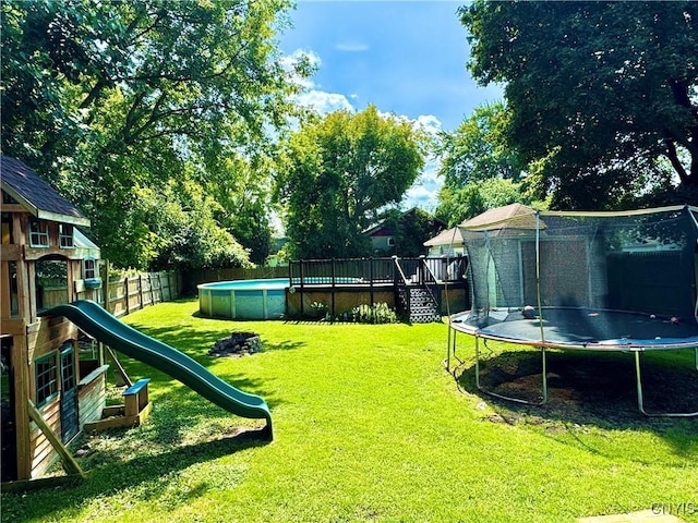 view of yard featuring a deck, a playground, a fenced backyard, a fenced in pool, and a trampoline