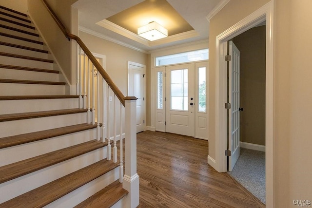 foyer with a raised ceiling, wood-type flooring, and ornamental molding