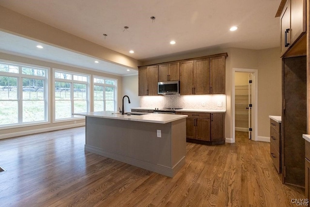 kitchen with stainless steel appliances, a kitchen island with sink, decorative backsplash, and hardwood / wood-style flooring