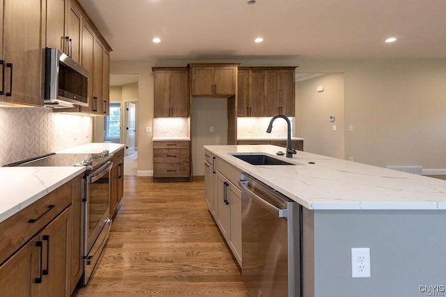 kitchen with a kitchen island with sink, appliances with stainless steel finishes, wood-type flooring, and decorative backsplash