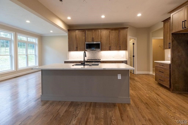 kitchen with a kitchen island with sink, sink, light hardwood / wood-style flooring, and decorative backsplash