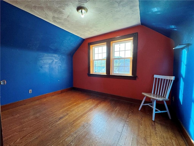 additional living space with baseboards, vaulted ceiling, a textured ceiling, and wood finished floors