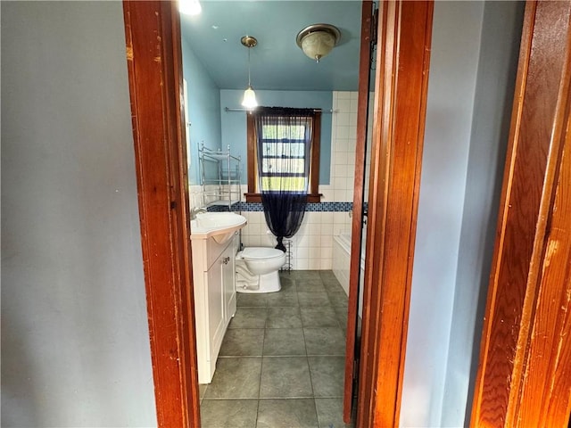 bathroom with toilet, vanity, tile walls, wainscoting, and tile patterned floors