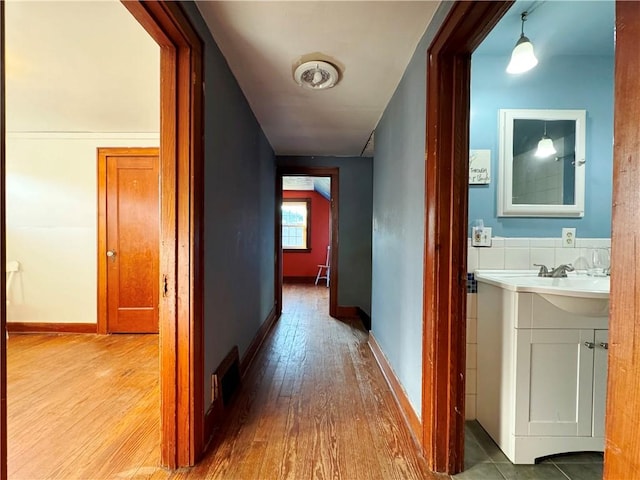 hallway with visible vents, baseboards, and wood finished floors