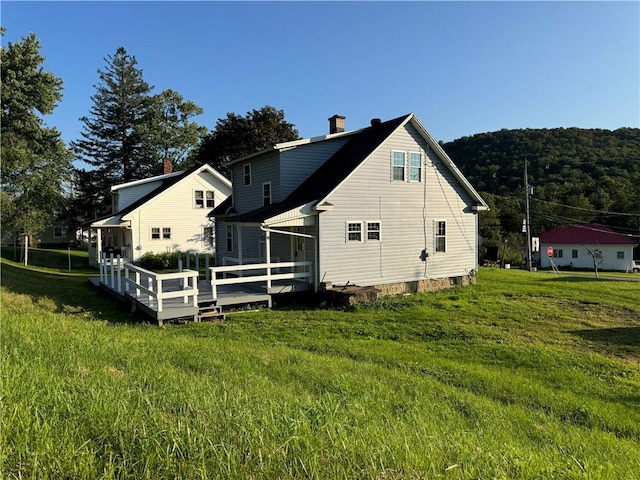 rear view of house with a yard, a chimney, and a wooden deck