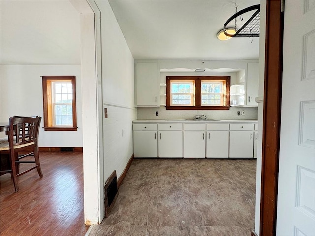 kitchen featuring baseboards, visible vents, white cabinets, and a sink