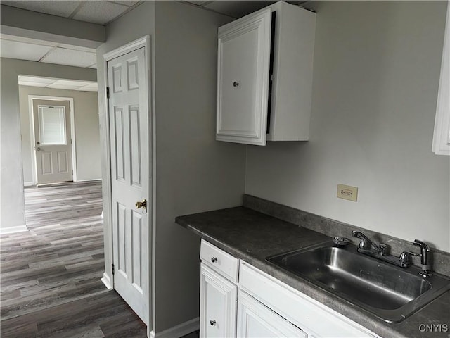 kitchen featuring dark wood-style flooring, dark countertops, white cabinetry, a sink, and a drop ceiling