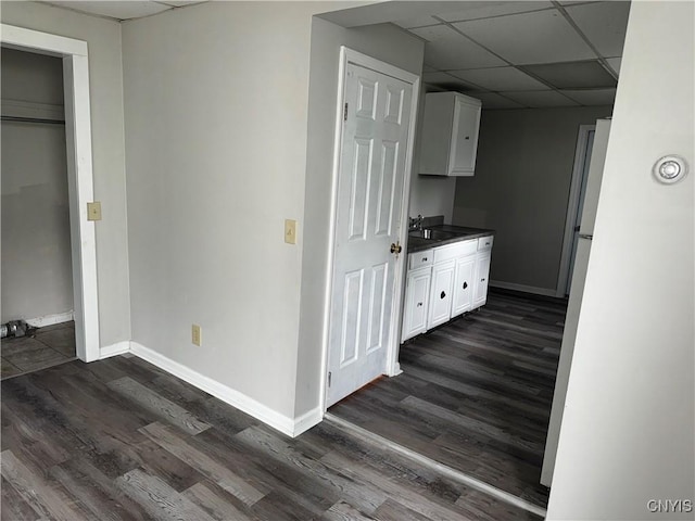 interior space featuring dark wood-type flooring, a sink, a paneled ceiling, and baseboards