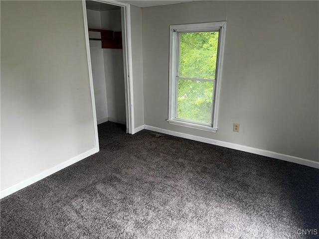 unfurnished bedroom with baseboards, dark carpet, and a closet