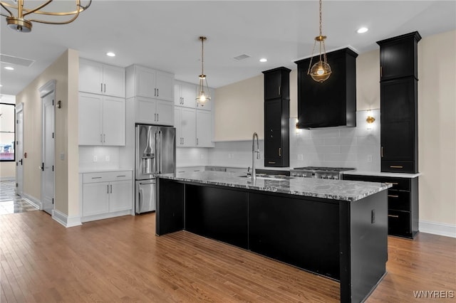 kitchen featuring light wood-type flooring, a center island with sink, backsplash, and high end fridge