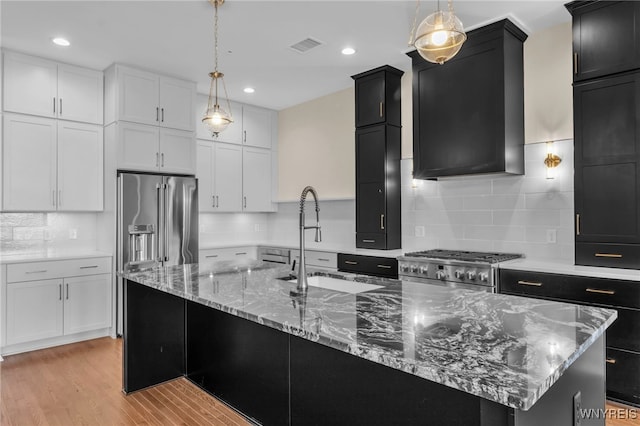 kitchen featuring light wood-type flooring, a kitchen island with sink, decorative backsplash, and high end refrigerator