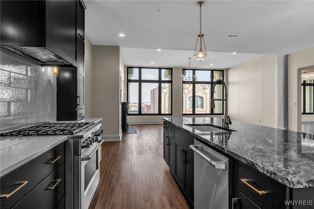 kitchen with sink, appliances with stainless steel finishes, dark wood-type flooring, decorative backsplash, and an island with sink