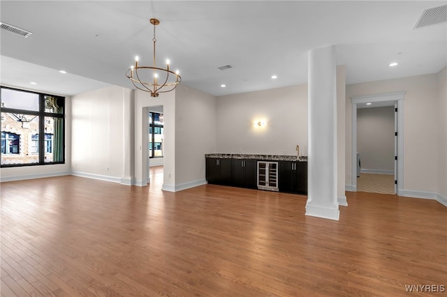 unfurnished living room with hardwood / wood-style flooring, decorative columns, beverage cooler, and a chandelier