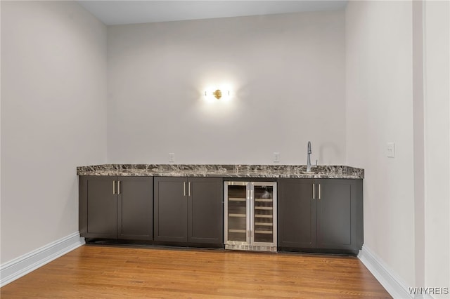 bar with light wood-type flooring, wine cooler, sink, and light stone countertops