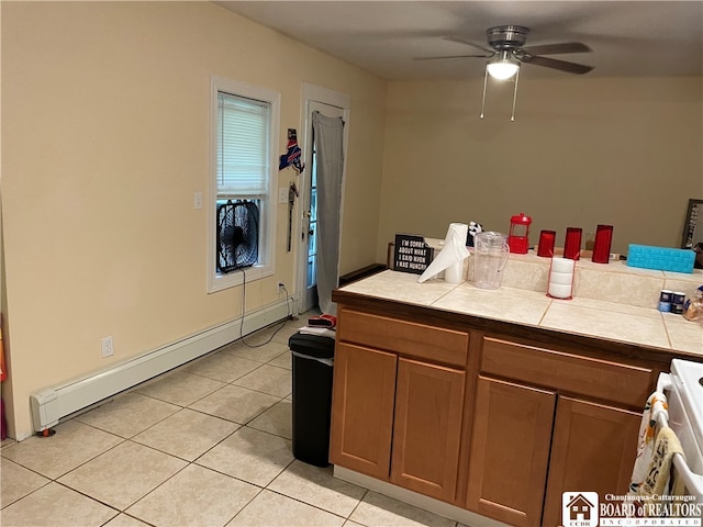 kitchen with light tile patterned flooring, white range, ceiling fan, a baseboard radiator, and tile counters