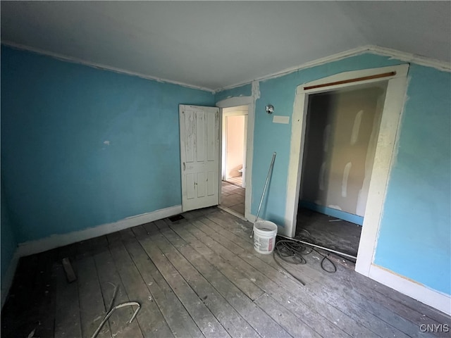 unfurnished bedroom featuring hardwood / wood-style flooring, a closet, vaulted ceiling, and ornamental molding