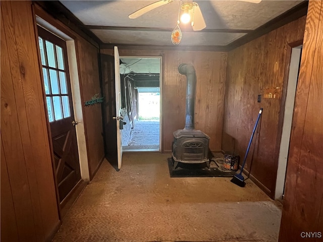 interior space with wood walls, ceiling fan, and a wood stove