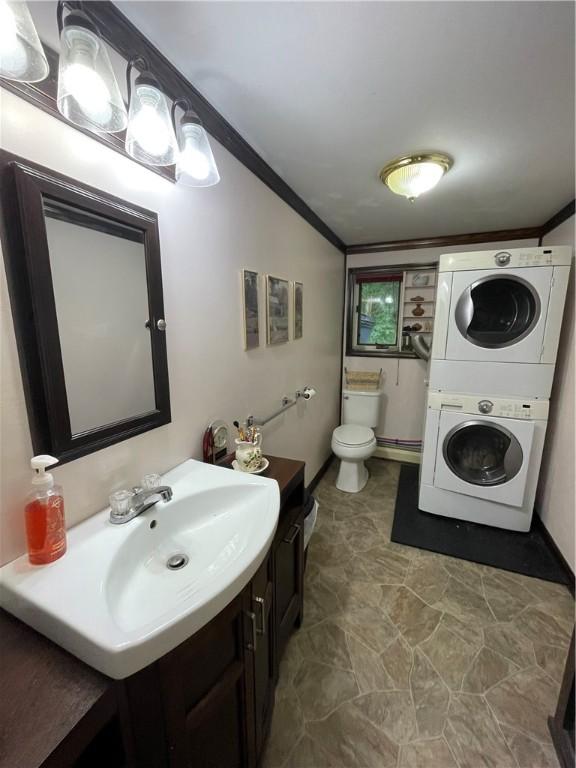 bathroom with stacked washer / dryer, crown molding, vanity, and toilet