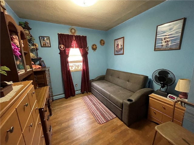 sitting room with a baseboard radiator, a textured ceiling, and light wood-type flooring