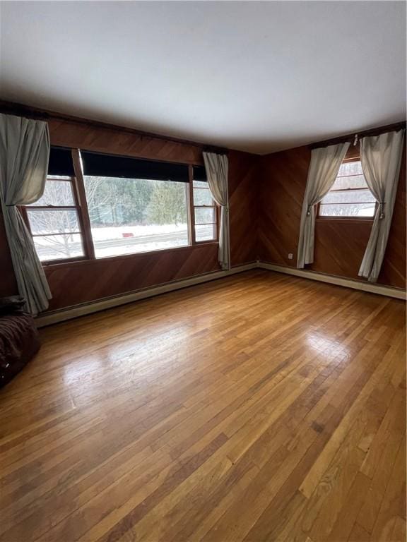 unfurnished room featuring a baseboard radiator, wood walls, and wood-type flooring